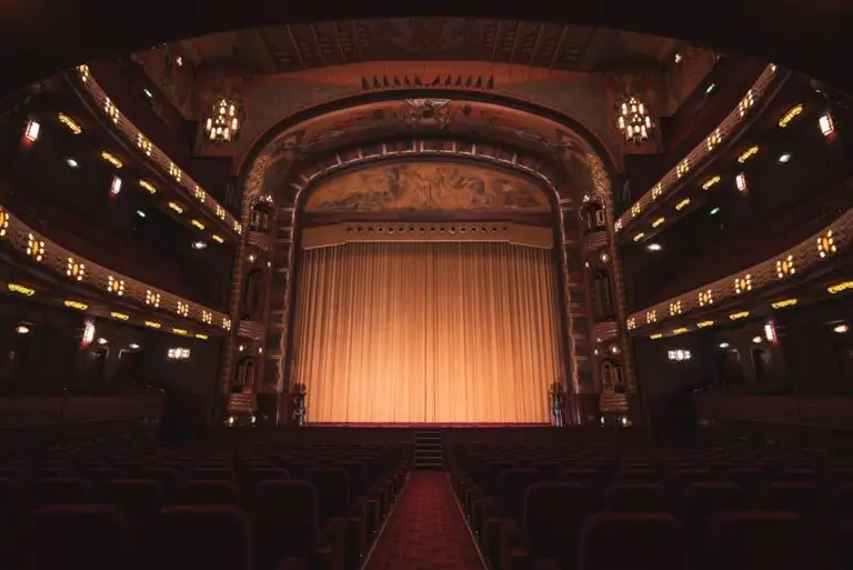 Empty theater with red seats facing a gold stage curtain